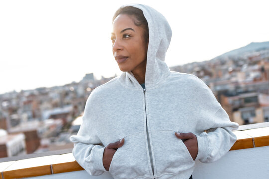 Athletic woman in a hoodie on a rooftop overlooking cityscape