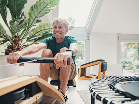 Smiling person rowing on fitness machine at home in living room