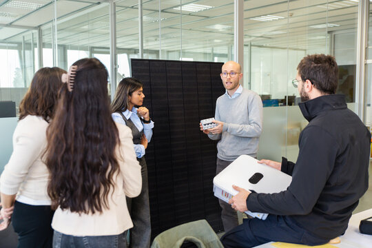 Office team collaborating with employee presenting solar panel battery