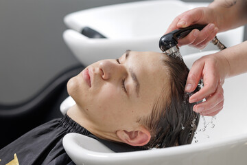 Naklejka premium Hairdresser rinsing boy hair with water at salon sink close up
