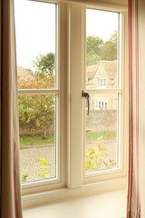 Fototapeta premium Window view looking out to a charming English Cotswold village with stone houses and autumn trees