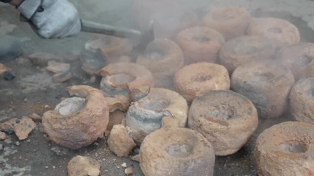 A worker using a hammer to break open cooled clay molds to reveal the cast metal pieces inside