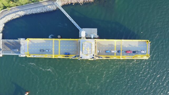 Yellow open deck island car ferry loading vehicles at a road loading ramp in Finnish archipelago. Aerial top down view.