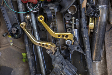 Fototapeta premium Chaotic pile featuring gold motorcycle brake lever part resting on dirty metal scrap in rough mechanic garage feeling abandoned and gritty amidst various discarded mechanical hardware component