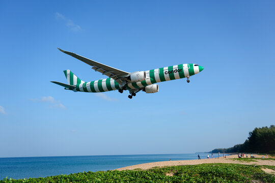 Condor airways airbus a330 green striped landing above beautiful beach with people on the beach and sea, travel. Thailand, Phuket International airport. 10 March 2026.