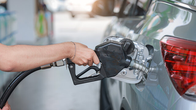 Person uses pump to put gasoline into vehicle tank feeling stressed by rising fuel cost during local service station visit