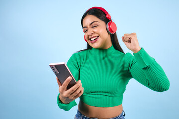 young latina woman listening to music and using headphones on blue background in Mexico Latin America, Mexican young brunette female portrait © Marcos