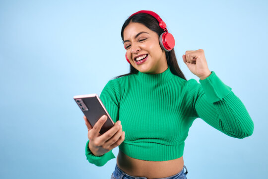 young latina woman listening to music and using headphones on blue background in Mexico Latin America, Mexican young brunette female portrait