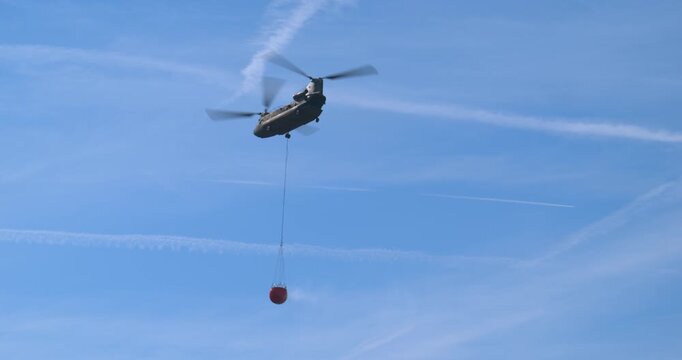 Transport helicopter of Dutch Royal Air Force carrying a water bucket for extinguishing wildfires in nature.