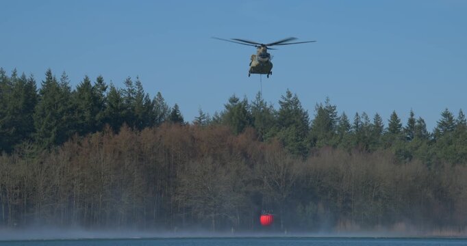 Transport helicopter of Dutch Royal Air Force carrying a water bucket for extinguishing wildfires in nature.