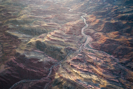 Aerial view of the winding, sandy river cutting through the rugged, multi-hued terrain, a tapestry of earth tones painted under the vast sky, Indio, California, United States.