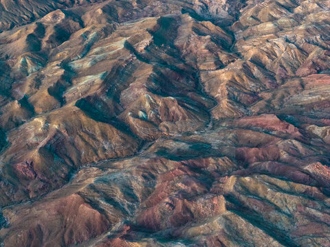 Aerial view of the rugged, undulating terrain, where the earth's crust folds in a symphony of ochre, rust, and umber hues, a testament to nature's artistry, Indio, California, United States.
