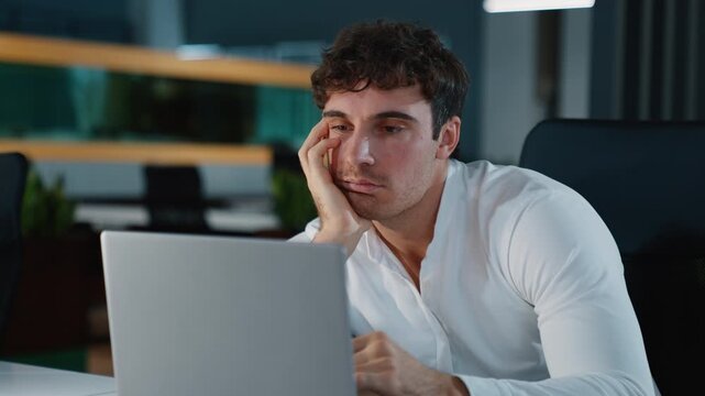 Overworked Caucasian tired business man working with laptop difficult job overload businessman male specialist guy professional fatigue work with computer monotone boring task in night evening office