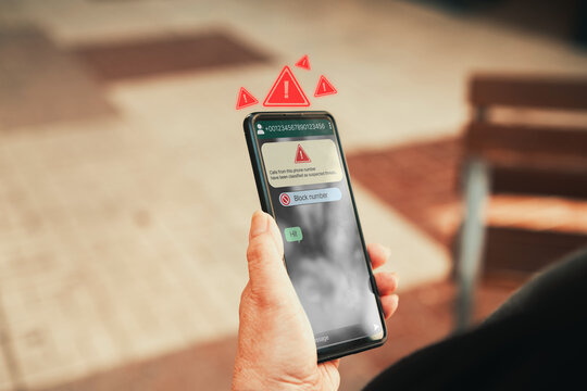 Spam text message warning on smartphone screen. Woman hand holding phone with scam alert. Phishing and cybersecurity concept.