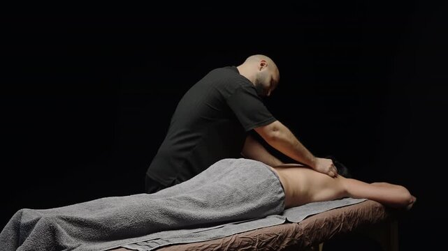 Professional massage therapist performing deep tissue back massage on a draped client in a tranquil studio, using forearm and hand techniques to relieve tension and promote relaxation against a dark