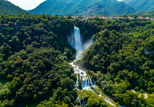 Aerial view of the cascading Marmore Falls plunging through the verdant forest, a symphony of white water against the deep green canopy, Terni, Umbria, Italy.