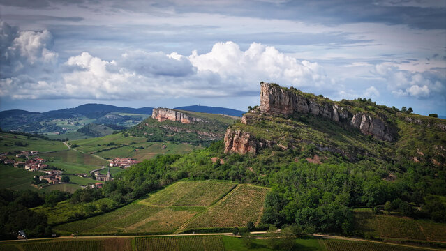 Aerial view of verdant vineyards stretching towards dramatic rocky outcrops under a brooding sky, Solutre-Pouilly, France.
