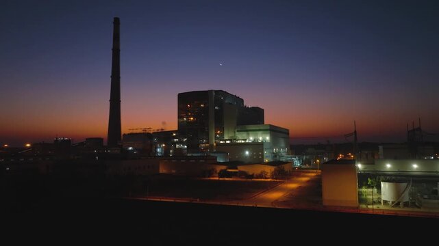 Forward aerial ascent looking at Thar Coal Power Plant during afterglow with industrial lights on and a hazy horizon in Pakistan.