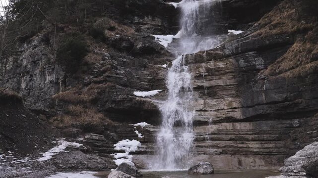 Beautiful waterfall cascading over rocky cliffs in the Austrian Alps with patches of winter snow
