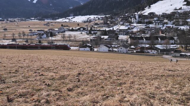 Red train passing through the alpine village of Lermoos, Austria, with mountains and melting snow
