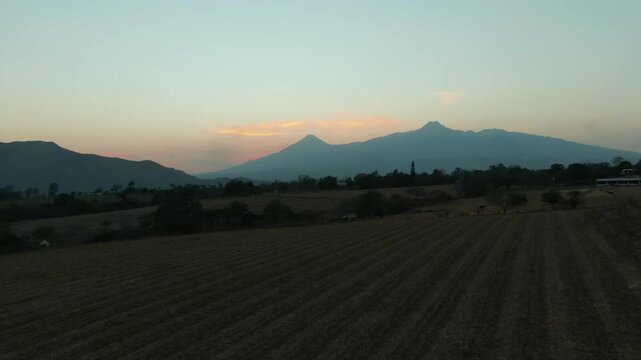 Colima Volcanos rising above agricultural land in Tuxpan, Jalisco at sunset in aerial view