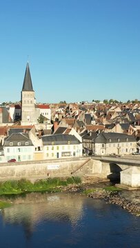 Scenic view of La Charite sur Loire with traditional rooftops, a church tower, and a stone bridge over the river under clear blue sky.