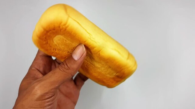 Hand motion displaying a bright golden baked bread roll rotating slightly against a clean white background in this looped food preparation video footage.