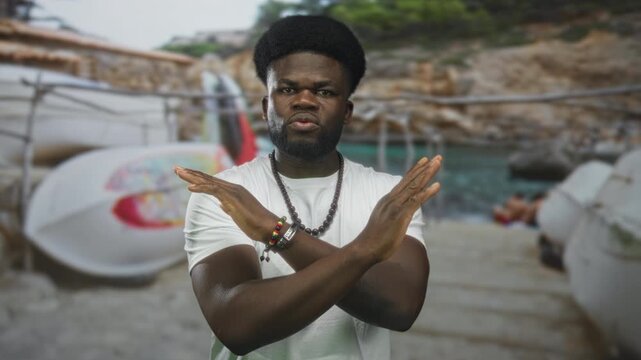 Man with arms crossed in street showing hands and bracelets wearing white t shirt and beads; refusal.