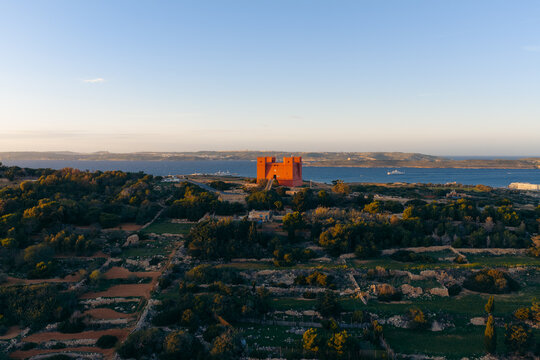 Aerial view of the vibrant Red Tower standing boldly against the serene blue horizon and contrasting with the lush greenery, Il-Mellieha, Red Tower, Malta.