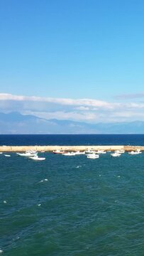 Small fishing boats float in a tranquil harbor with clear blue water and distant mountains under a bright sky in Koroni, Greece.