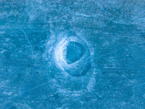 Aerial view of a mesmerizing frozen expanse with a circular opening revealing the water beneath, a stark contrast of icy blues and liquid depths, Elk, Warmian-Masurian Voivodeship, Poland.