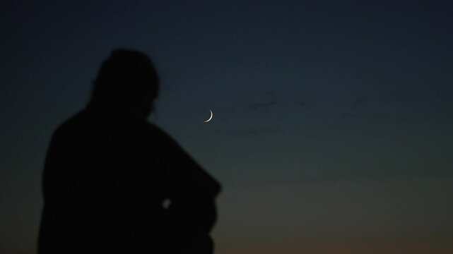 Woman silhouette walking into frame of crescent moon in the night sky lunar phase