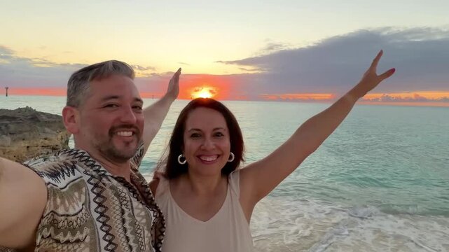 Happy mid adult latin heterosexual couple embracing and smiling for a sunset selfie on a Bahamas pier during their romantic honeymoon vacation, warm tropical light and joyful togetherness.