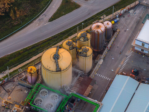 Aerial view of industrial tanks gleaming under the diffused light, contrasting against the stark asphalt and verdant greenery, Vasto, Abruzzo, Italy.