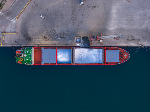 Aerial view of a vibrant cargo ship docked along the concrete pier, contrasting with the deep blue sea, Vasto, Abruzzo, Italy.