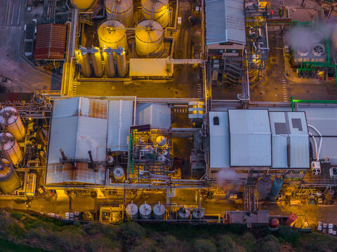 Aerial view of an industrial plant, its tanks gleaming under the dim light, painting a stark contrast against the darkening sky, Vasto, Abruzzo, Italy.