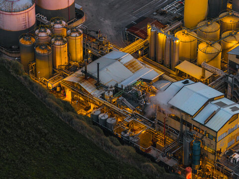 Aerial view of an industrial landscape where silver tanks gleam under warm, artificial lights against the dark, angular architecture and a touch of green vegetation, Vasto, Abruzzo, Italy.