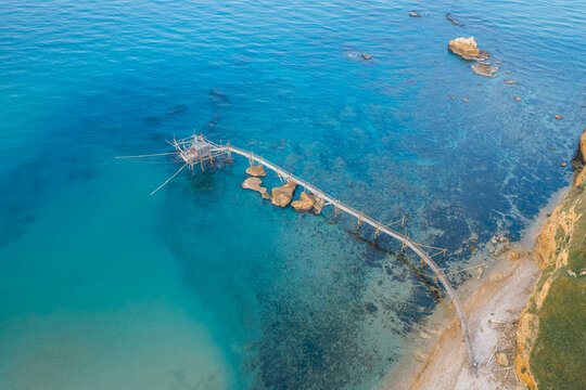 Aerial view of a trabucco stretching into the turquoise sea contrasting with the rugged coastline, Punta Aderci, Vasto, Abruzzo, Italy.