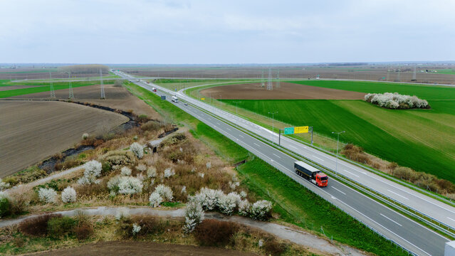 Aerial view of a long straight highway cutting through a rural landscape with fields of green and brown, punctuated by power lines, , Sremska Mitrovica, Vojvodina, Serbia.