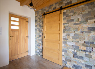 Top hung hanging wooden barn sliding door with a grey brick wall © Anita