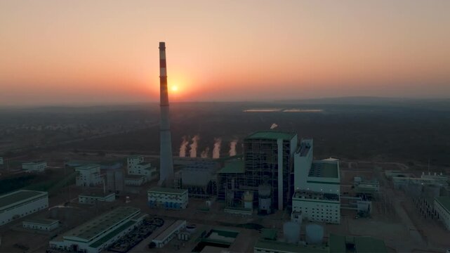 High aerial at Thar Coal Power Plant in Pakistan as the sun sets, with the large chimney passing over the sun's rays.
