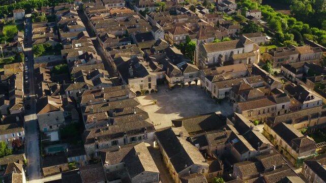 Empty central square of the Bastide de Monpazier surrounded by historic stone architecture and arcade houses. High angle drone shot.
