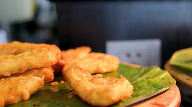 a street vendor cooks assorted sweet snack fried bananas. a fresh batch of crispy banana fritters drains in a metal basket, showcasing their golden-brown coating and crunchy texture. Indonesian snacks