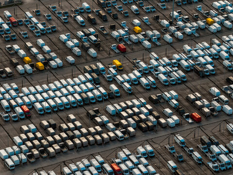Aerial view of tightly packed vehicles, a symphony of whites, punctuated by vibrant yellows and reds, filling the frame with an industrial rhythm, Atessa, Abruzzo, Italy.
