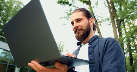 Portrait of focused business man in a formal suit working remotely on a wireless laptop while...