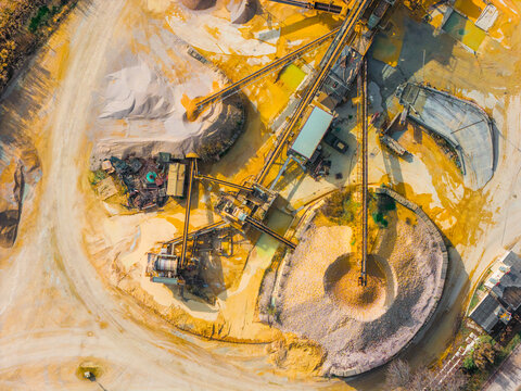 Aerial view of an industrial quarry site, a tableau of ochre earth, concrete, and metallic structures under the sun's glare, Atessa, Abruzzo, Italy.