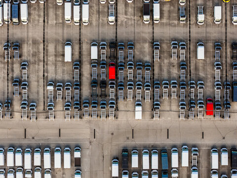 Aerial view of countless vehicles neatly arranged in rows, punctuated by the striking contrast of a few vibrant red vans, Atessa, Abruzzo, Italy.