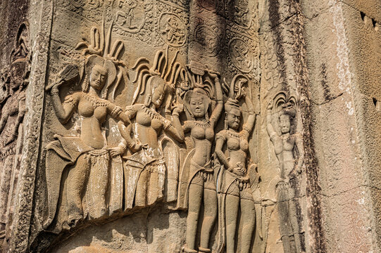 Ancient weathered stone wall featuring intricate bas-relief carvings of celestial Apsara dancers at historic Angkor Wat temple complex in sunny Cambodia