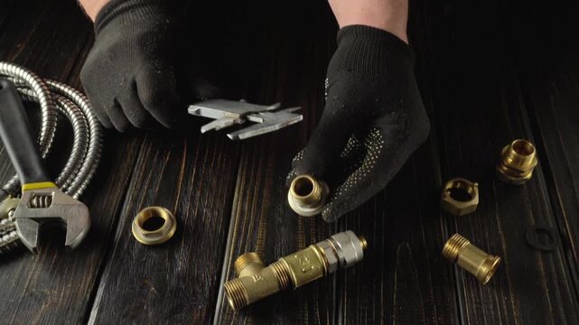 Technician measures brass fittings with calipers while surrounded by plumbing components on a wooden work surface in a well-lit workshop