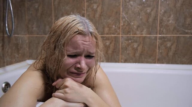 Psychological suffering, mental crisis, loneliness or domestic abuse. Blonde woman sitting in bathtub with streaming tears, smeared mascara, sorrowful eyes, tiled bathroom, despair, depression